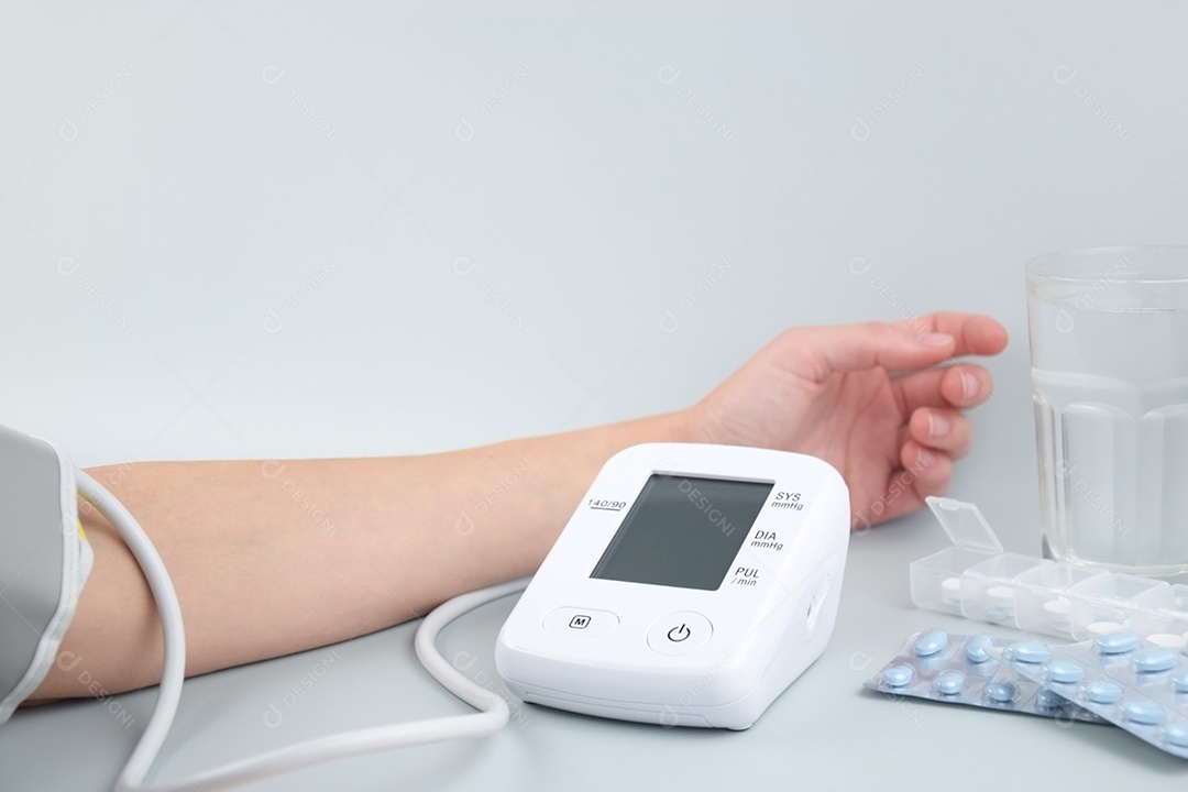 Aparelho digital de pressão arterial no braço e comprimidos em um fundo claro