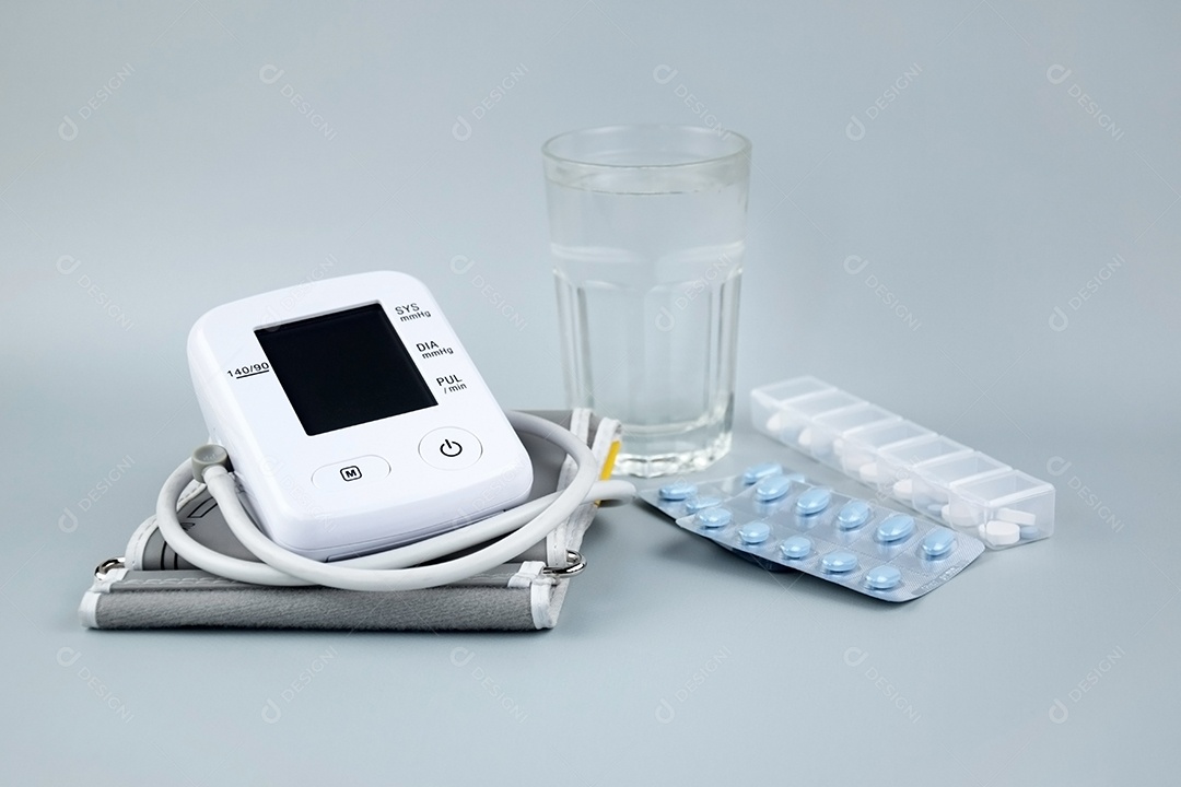 Aparelho digital de pressão arterial e comprimidos copo de vidro em um fundo claro