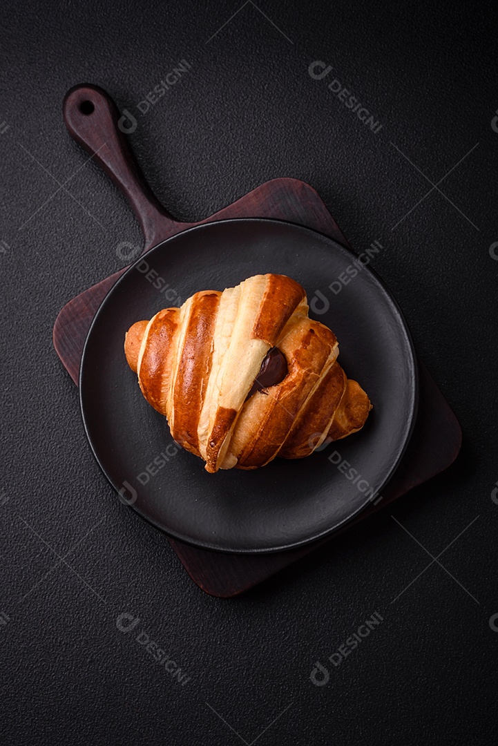 Deliciosa corneta de croissant doce e crocante com chocolate sobre um fundo escuro de concreto