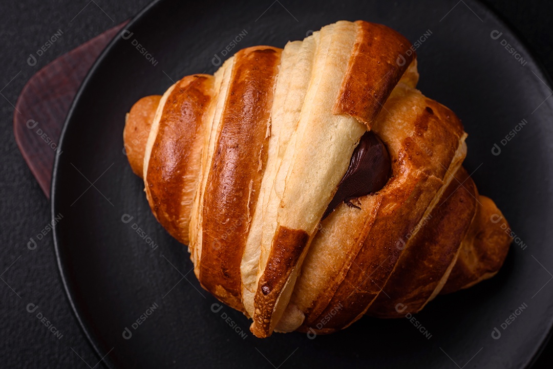 Deliciosa corneta de croissant doce e crocante com chocolate sobre um fundo escuro de concreto