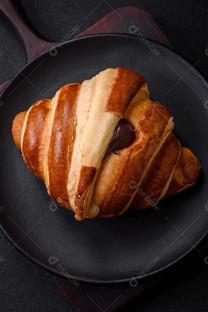 Deliciosa corneta de croissant doce e crocante com chocolate sobre um fundo escuro de concreto