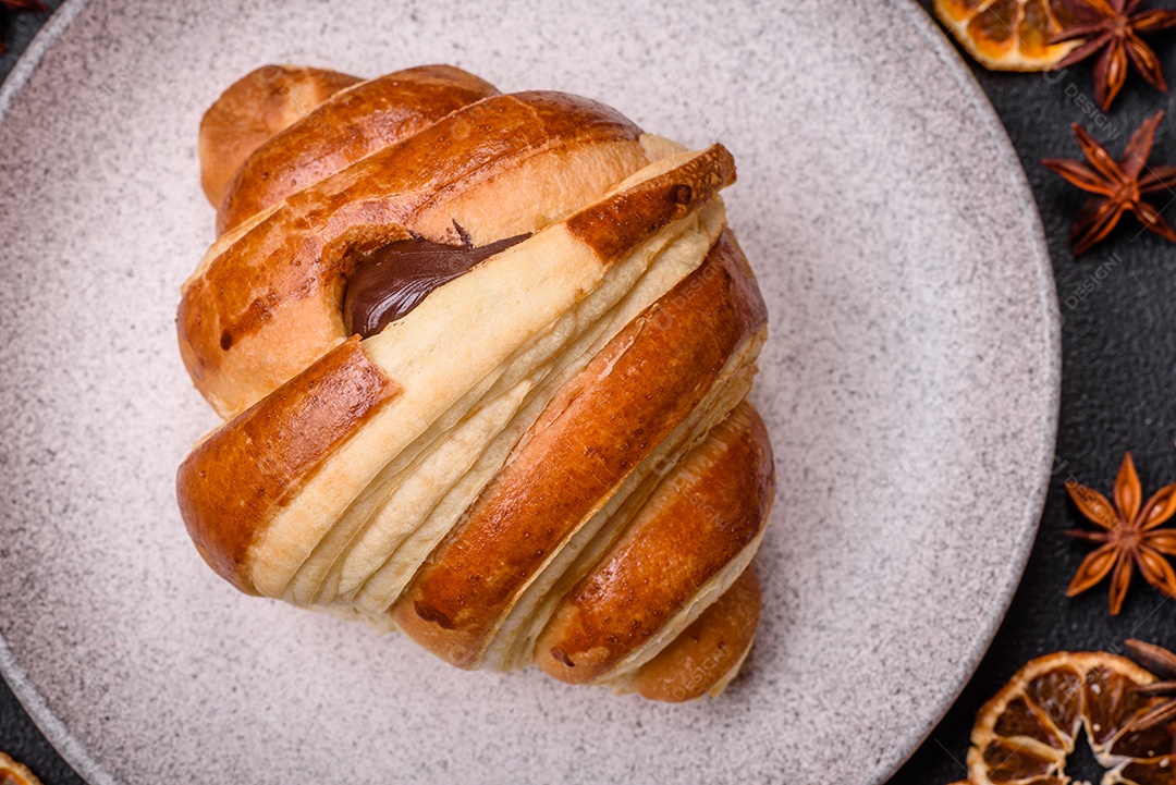 Deliciosa corneta de croissant doce e crocante com chocolate sobre um fundo escuro de concreto