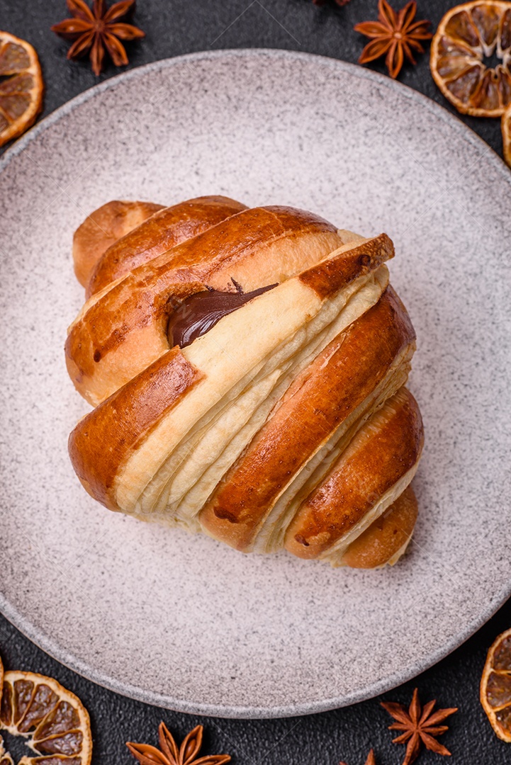 Deliciosa corneta de croissant doce e crocante com chocolate sobre um fundo escuro de concreto