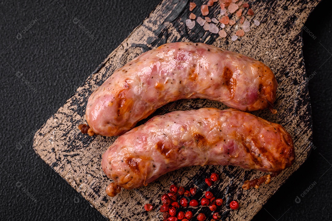 Deliciosas salsichas grelhadas de frango ou porco com sal e especiarias sobre um fundo escuro de concreto