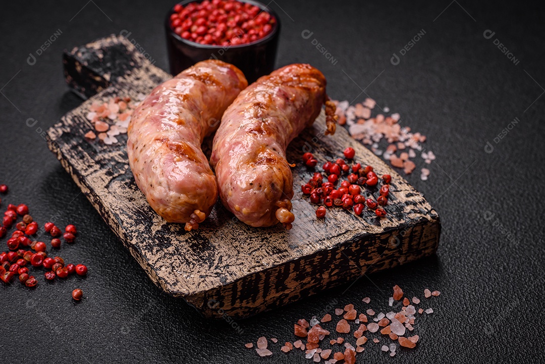 Deliciosas salsichas grelhadas de frango ou porco com sal e especiarias sobre um fundo escuro de concreto