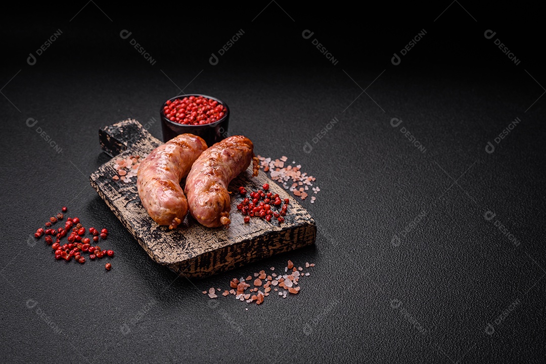 Deliciosas salsichas grelhadas de frango ou porco com sal e especiarias sobre um fundo escuro de concreto