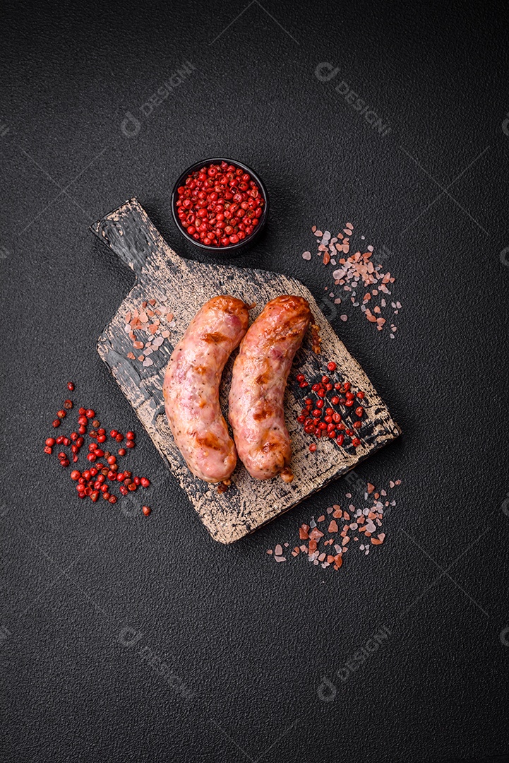 Deliciosas salsichas grelhadas de frango ou porco com sal e especiarias sobre um fundo escuro de concreto