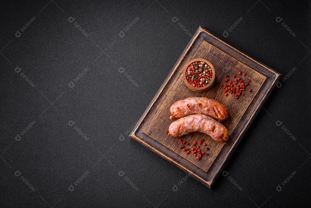Deliciosas salsichas grelhadas de frango ou porco com sal e especiarias sobre um fundo escuro de concreto