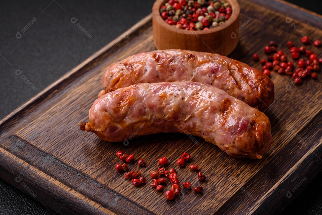 Deliciosas salsichas grelhadas de frango ou porco com sal e especiarias sobre um fundo escuro de concreto