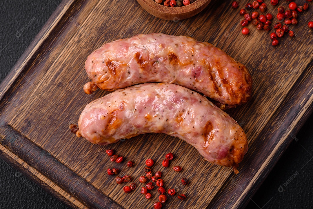 Deliciosas salsichas grelhadas de frango ou porco com sal e especiarias sobre um fundo escuro de concreto