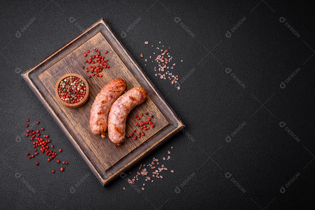 Deliciosas salsichas grelhadas de frango ou porco com sal e especiarias sobre um fundo escuro de concreto