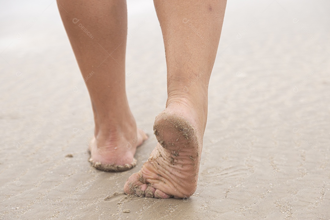 Pés de pessoa caminhando sobre praia