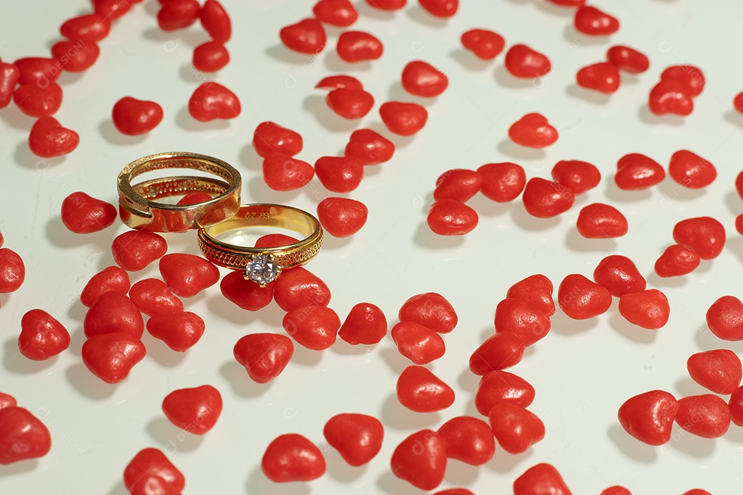Duas alianças de casamento com vários pequenos corações na mesa branca