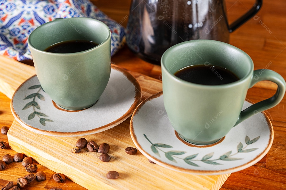 Duas xícaras de café e coador usado no fundo