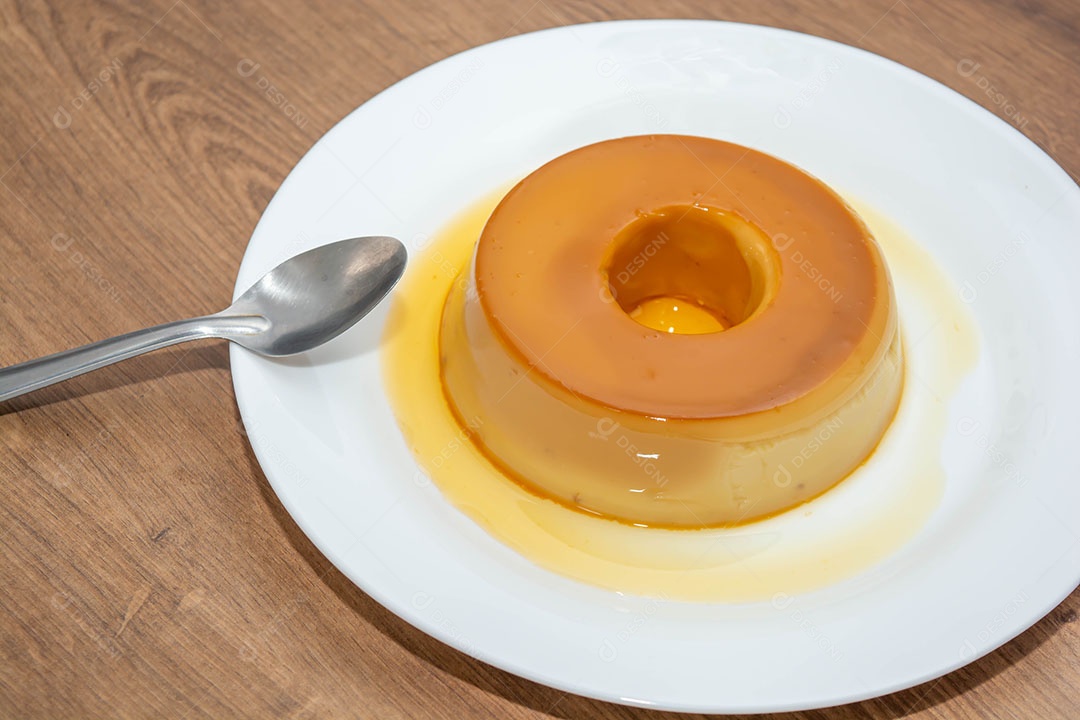 Pudim de leite em uma mesa de madeira com colher metálica