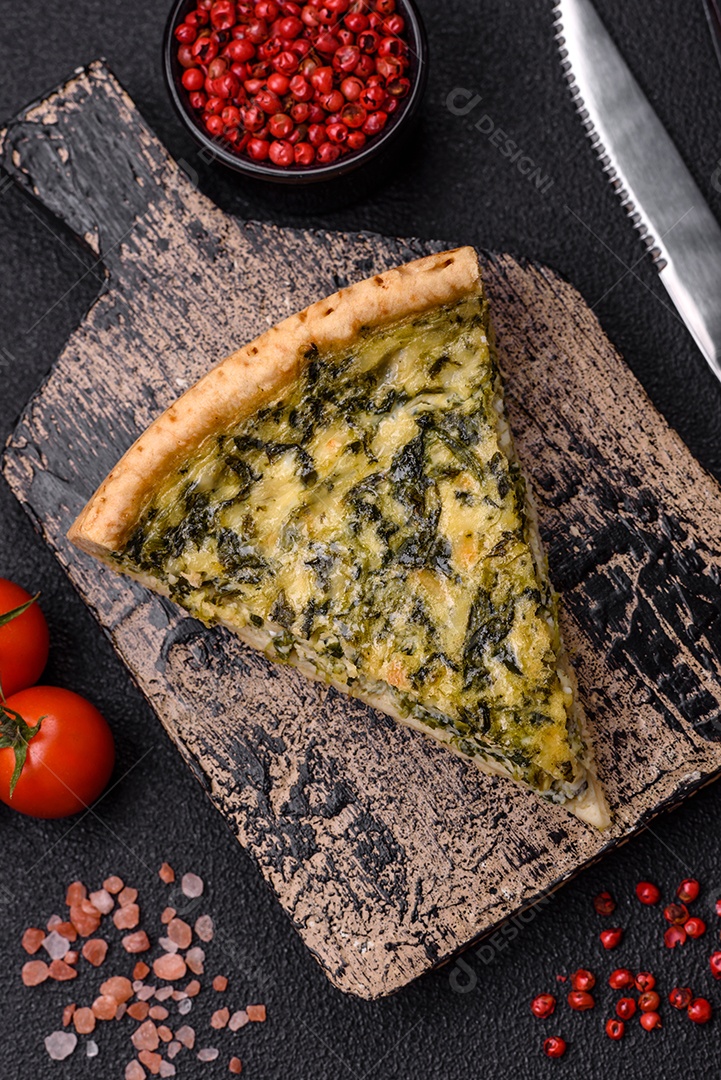 Deliciosa quiche crocante cortada em fatias com queijo, brócolis, tomate, sal, especiarias e ervas sobre um fundo escuro de concreto