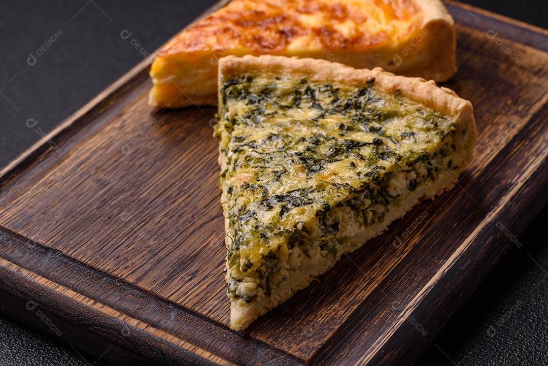 Deliciosa quiche crocante cortada em fatias com queijo, brócolis, tomate, sal, especiarias e ervas sobre um fundo escuro de concreto