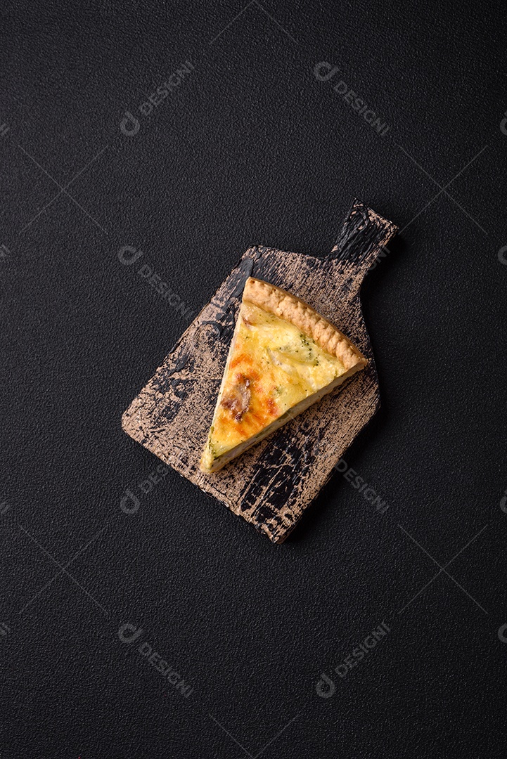 Deliciosa quiche crocante cortada em fatias com queijo, brócolis, tomate, sal, especiarias e ervas sobre um fundo escuro de concreto
