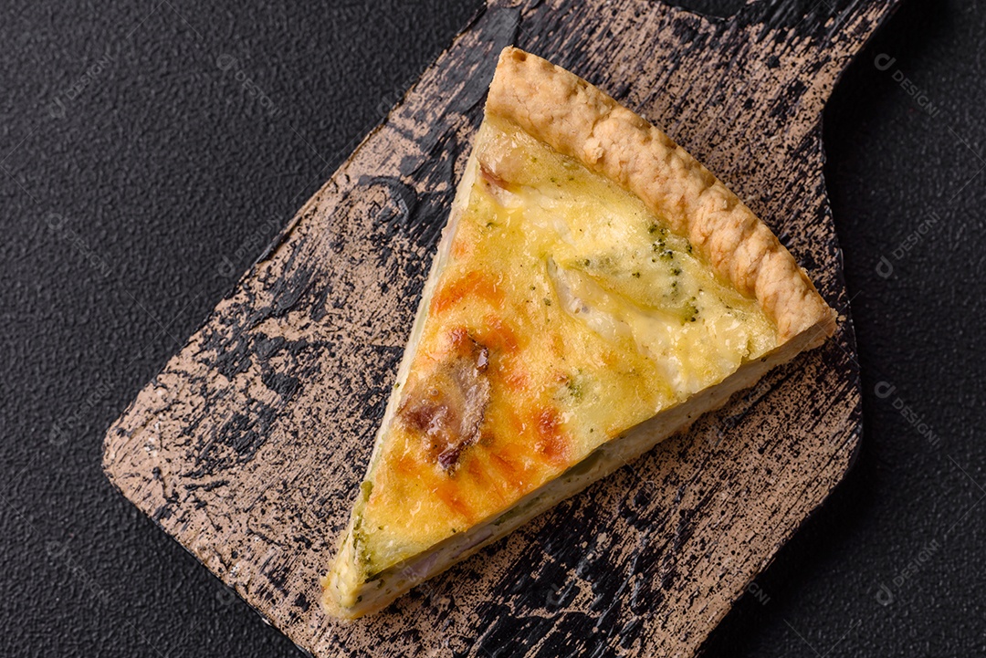Deliciosa quiche crocante cortada em fatias com queijo, brócolis, tomate, sal, especiarias e ervas sobre um fundo escuro de concreto