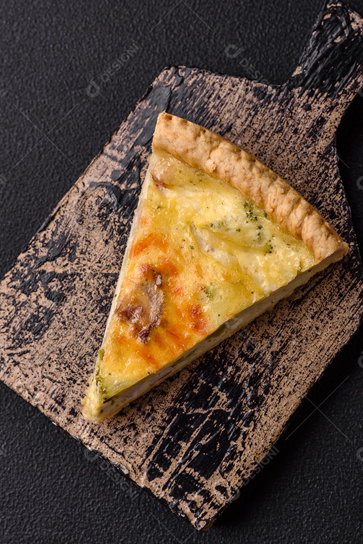 Deliciosa quiche crocante cortada em fatias com queijo, brócolis, tomate, sal, especiarias e ervas sobre um fundo escuro de concreto