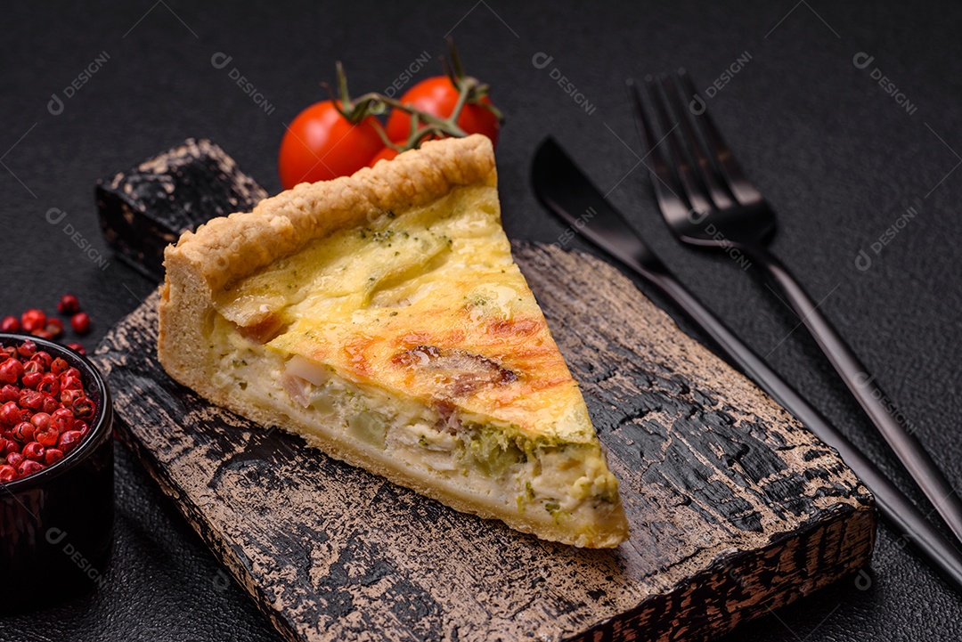 Deliciosa quiche crocante cortada em fatias com queijo, brócolis, tomate, sal, especiarias e ervas sobre um fundo escuro de concreto