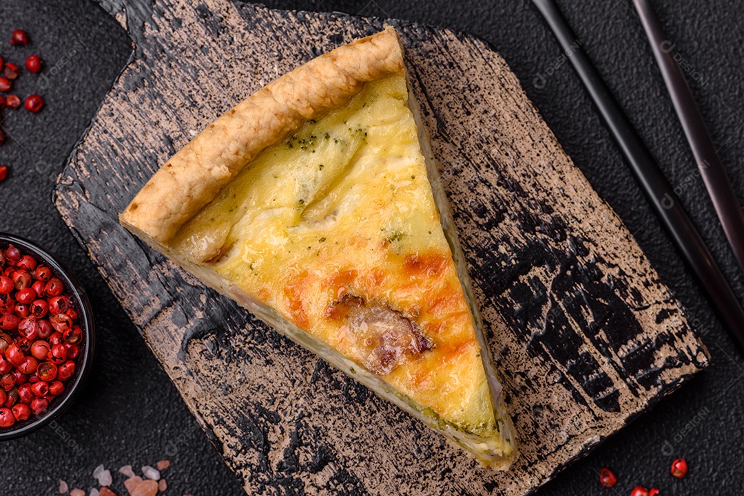 Deliciosa quiche crocante cortada em fatias com queijo, brócolis, tomate, sal, especiarias e ervas sobre um fundo escuro de concreto