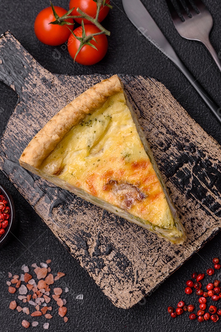 Deliciosa quiche crocante cortada em fatias com queijo, brócolis, tomate, sal, especiarias e ervas sobre um fundo escuro de concreto