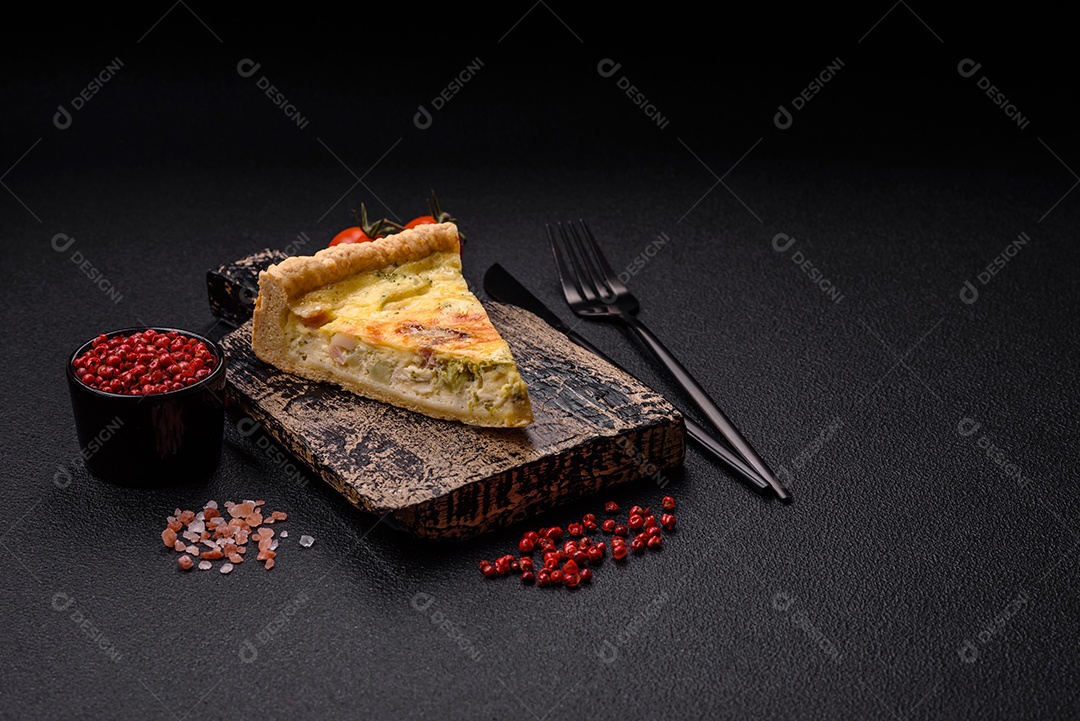 Deliciosa quiche crocante cortada em fatias com queijo, brócolis, tomate, sal, especiarias e ervas sobre um fundo escuro de concreto