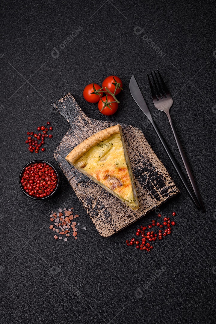 Deliciosa quiche crocante cortada em fatias com queijo, brócolis, tomate, sal, especiarias e ervas sobre um fundo escuro de concreto