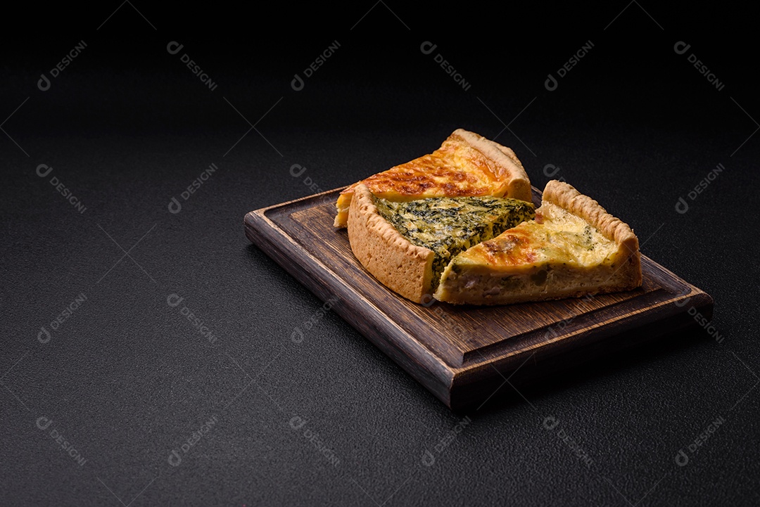 Deliciosa quiche crocante cortada em fatias com queijo, brócolis, tomate, sal, especiarias e ervas sobre um fundo escuro de concreto