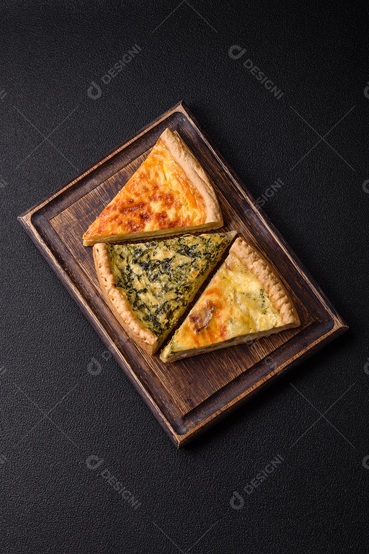 Deliciosa quiche crocante cortada em fatias com queijo, brócolis, tomate, sal, especiarias e ervas sobre um fundo escuro de concreto