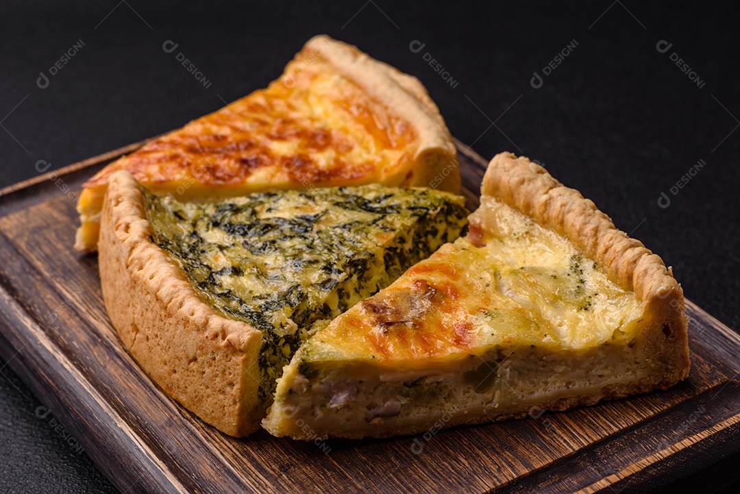Deliciosa quiche crocante cortada em fatias com queijo, brócolis, tomate, sal, especiarias e ervas sobre um fundo escuro de concreto