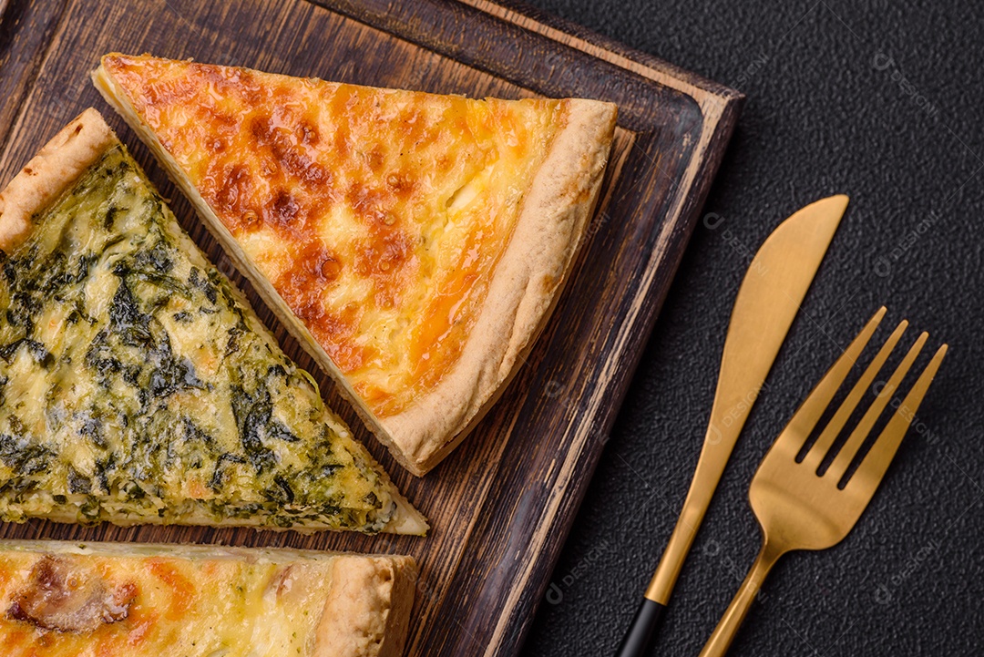 Deliciosa quiche crocante cortada em fatias com queijo, brócolis, tomate, sal, especiarias e ervas sobre um fundo escuro de concreto