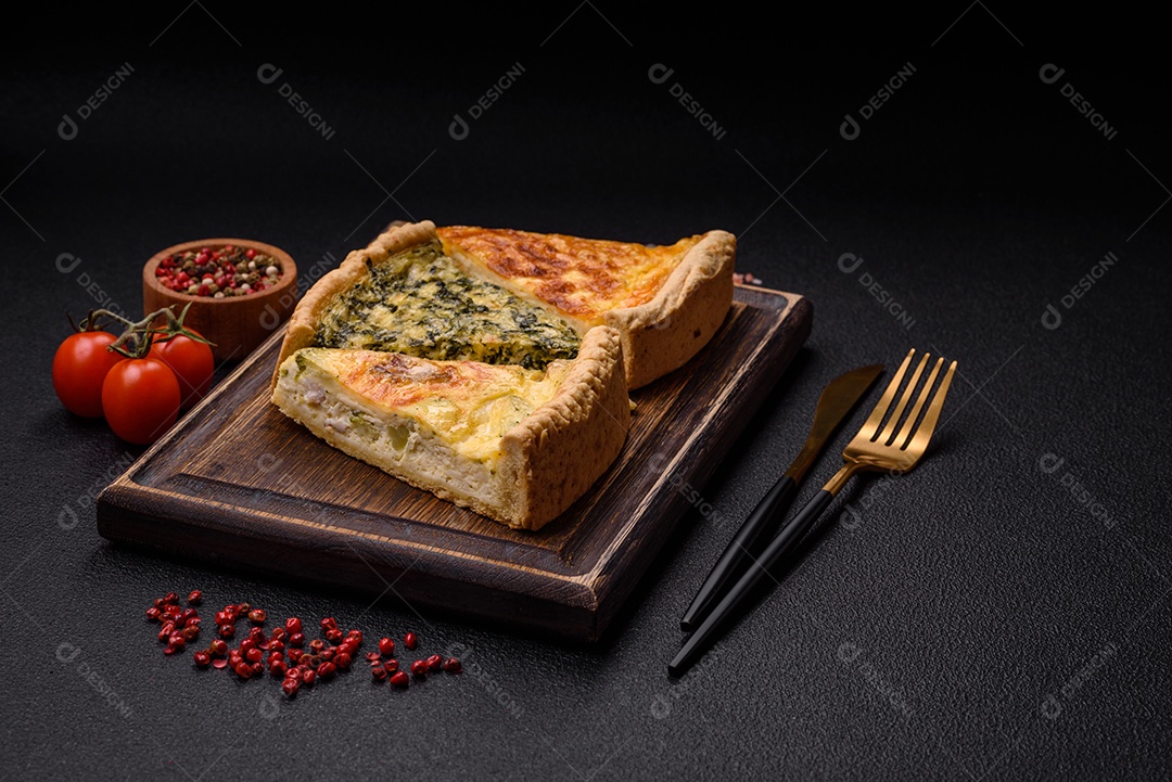 Deliciosa quiche crocante cortada em fatias com queijo, brócolis, tomate, sal, especiarias e ervas sobre um fundo escuro de concreto