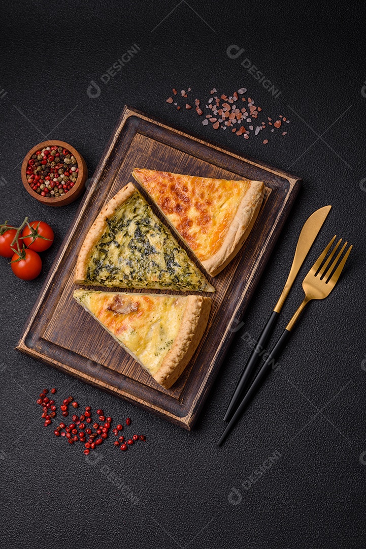 Deliciosa quiche crocante cortada em fatias com queijo, brócolis, tomate, sal, especiarias e ervas sobre um fundo escuro de concreto