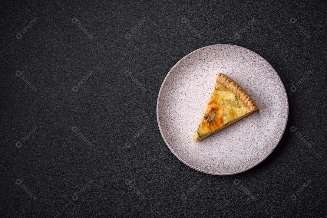 Deliciosa quiche crocante cortada em fatias com queijo, brócolis, tomate, sal, especiarias e ervas sobre um fundo escuro de concreto