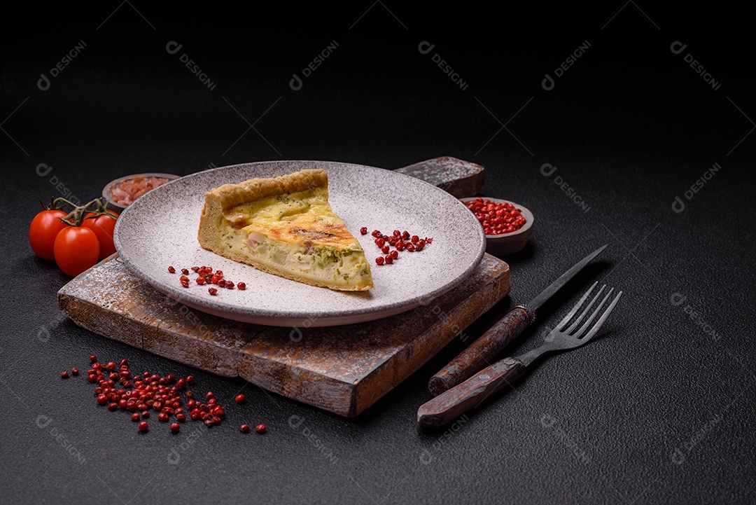 Deliciosa quiche crocante cortada em fatias com queijo, brócolis, tomate, sal, especiarias e ervas sobre um fundo escuro de concreto