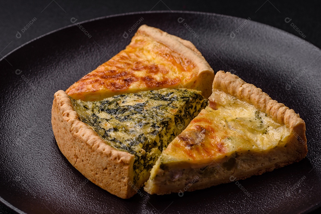 Deliciosa quiche crocante cortada em fatias com queijo, brócolis, tomate, sal, especiarias e ervas sobre um fundo escuro de concreto
