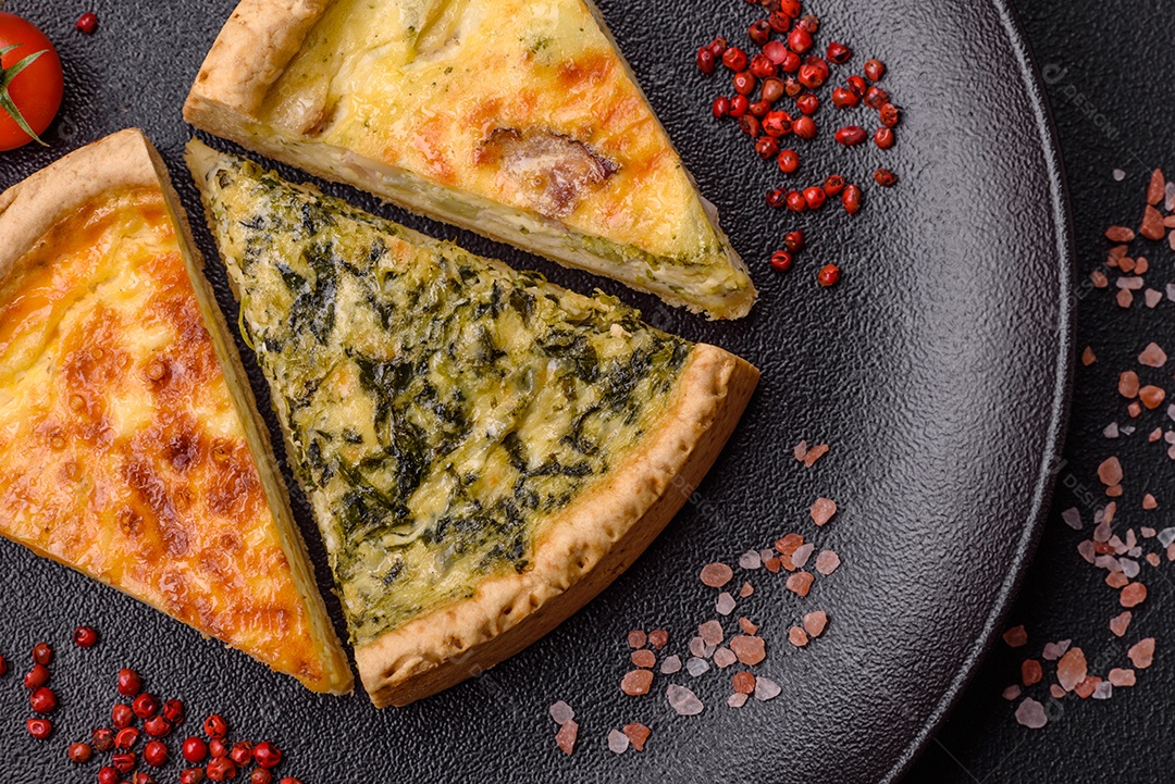 Deliciosa quiche crocante cortada em fatias com queijo, brócolis, tomate, sal, especiarias e ervas sobre um fundo escuro de concreto