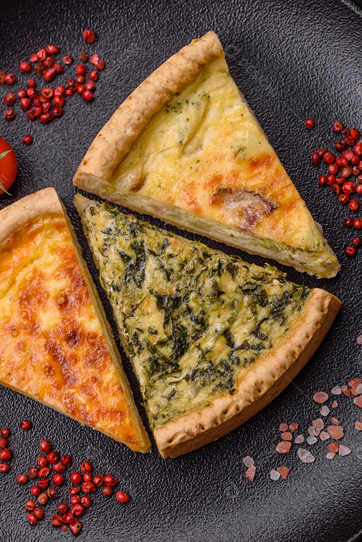 Deliciosa quiche crocante cortada em fatias com queijo, brócolis, tomate, sal, especiarias e ervas sobre um fundo escuro de concreto