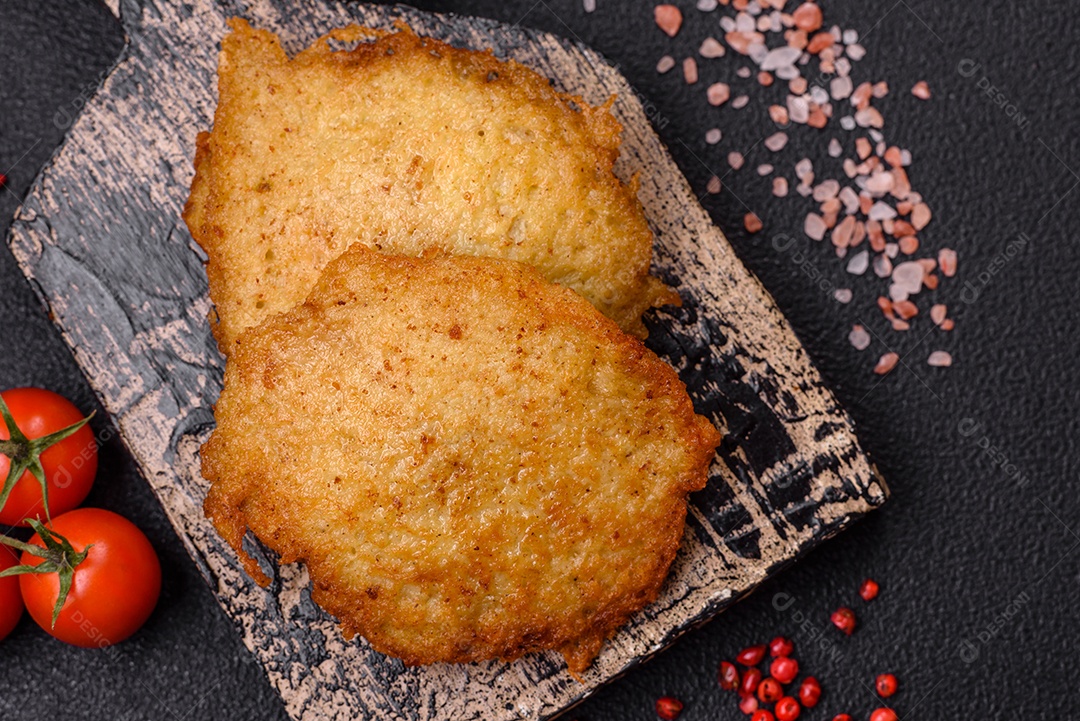 Deliciosas panquecas crocantes feitas de batatas, carne, cenouras, cebolas com sal, especiarias e ervas sobre um fundo escuro de concreto