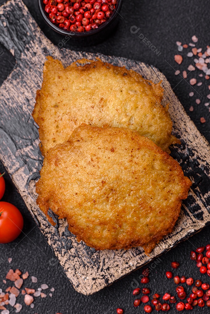 Deliciosas panquecas crocantes feitas de batatas, carne, cenouras, cebolas com sal, especiarias e ervas sobre um fundo escuro de concreto