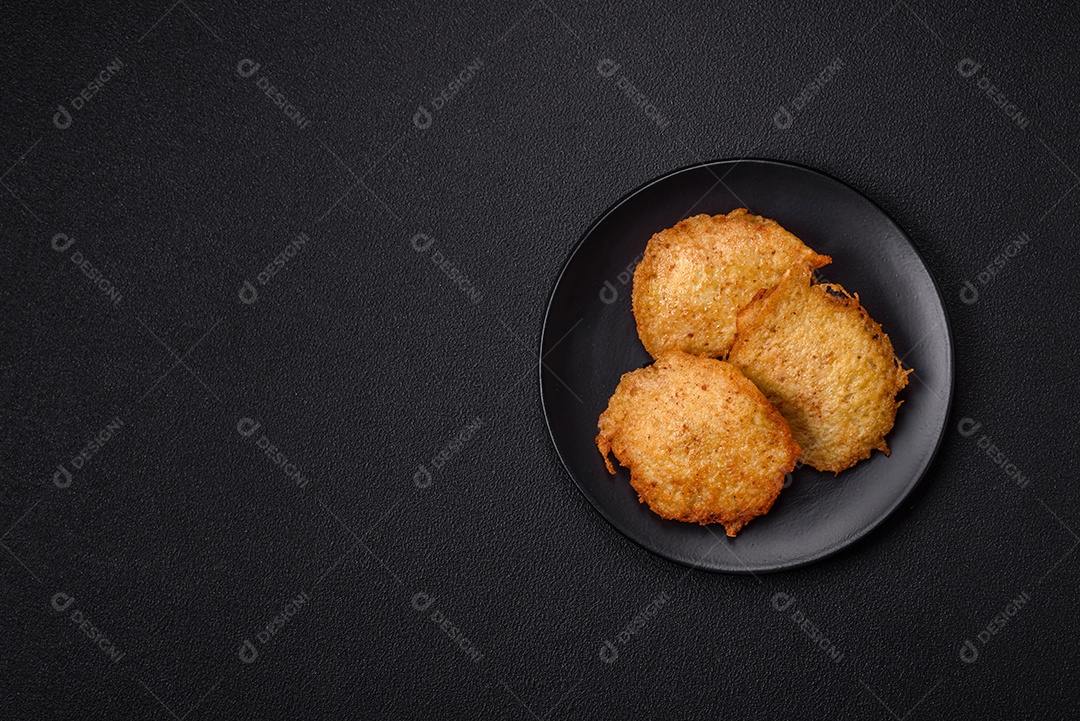 Deliciosas panquecas crocantes feitas de batatas, carne, cenouras, cebolas com sal, especiarias e ervas sobre um fundo escuro de concreto