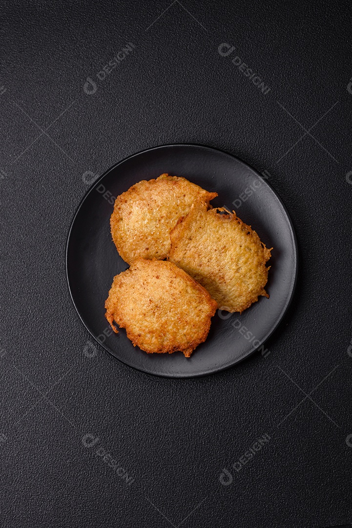 Deliciosas panquecas crocantes feitas de batatas, carne, cenouras, cebolas com sal, especiarias e ervas sobre um fundo escuro de concreto