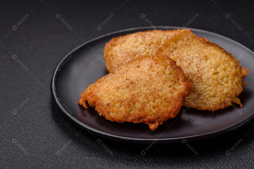 Deliciosas panquecas crocantes feitas de batatas, carne, cenouras, cebolas com sal, especiarias e ervas sobre um fundo escuro de concreto