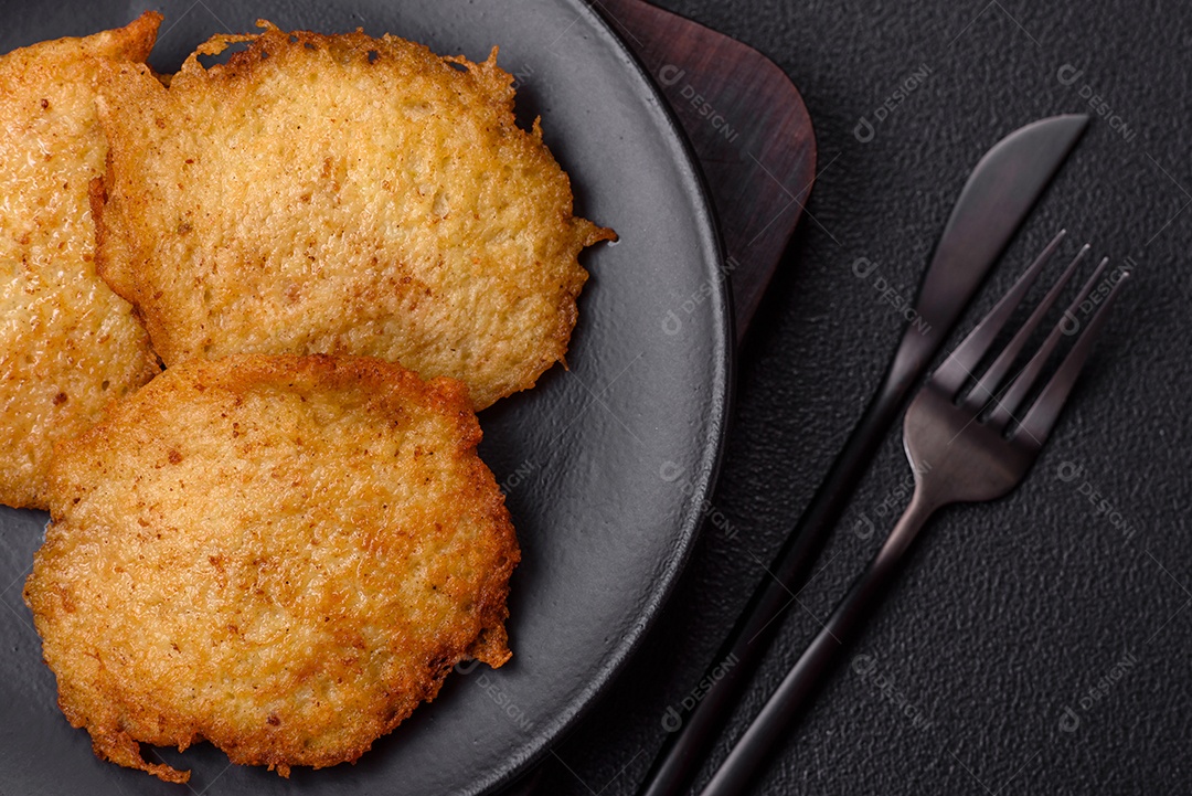 Deliciosas panquecas crocantes feitas de batatas, carne, cenouras, cebolas com sal, especiarias e ervas sobre um fundo escuro de concreto