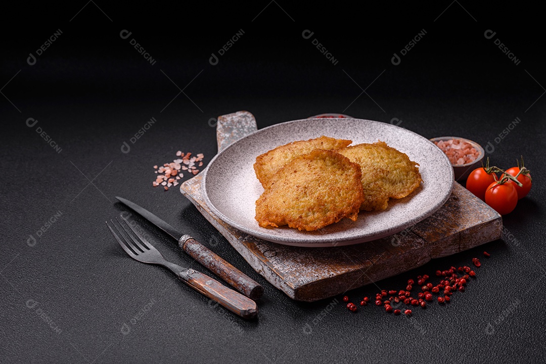 Deliciosas panquecas crocantes feitas de batatas, carne, cenouras, cebolas com sal, especiarias e ervas sobre um fundo escuro de concreto