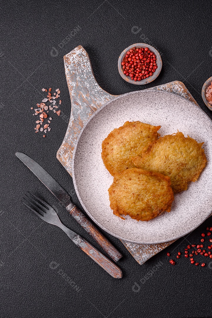 Deliciosas panquecas crocantes feitas de batatas, carne, cenouras, cebolas com sal, especiarias e ervas sobre um fundo escuro de concreto