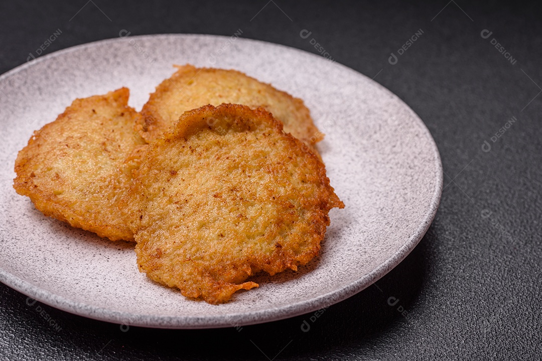 Deliciosas panquecas crocantes feitas de batatas, carne, cenouras, cebolas com sal, especiarias e ervas sobre um fundo escuro de concreto