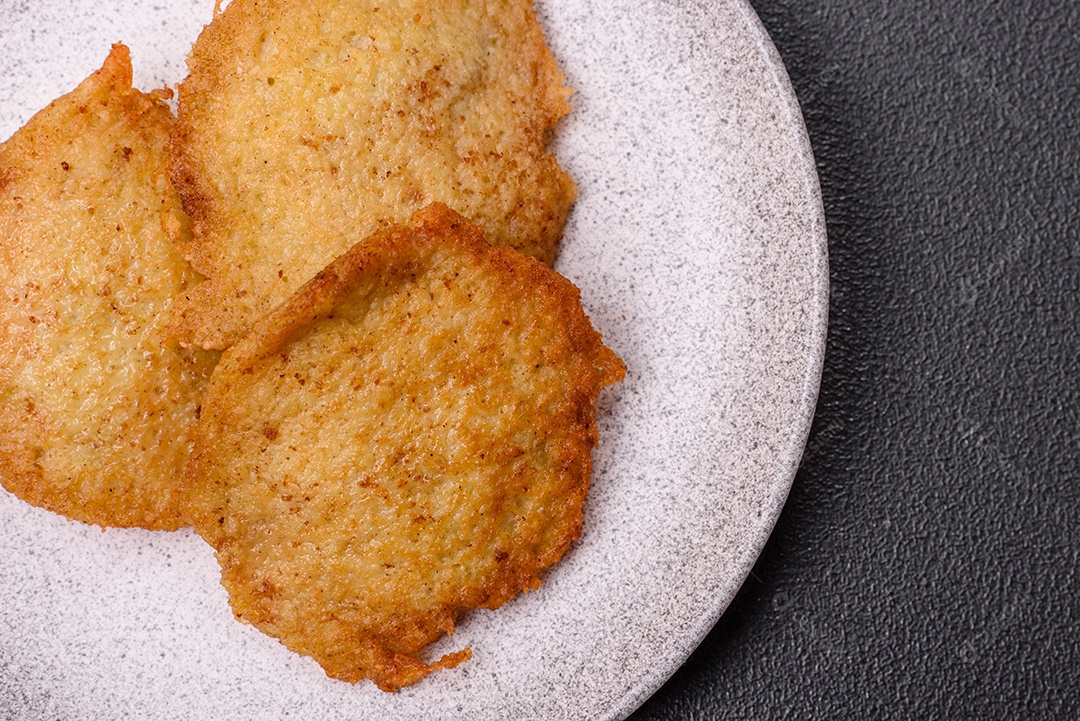 Deliciosas panquecas crocantes feitas de batatas, carne, cenouras, cebolas com sal, especiarias e ervas sobre um fundo escuro de concreto